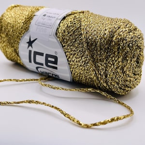 Peut inclure: Une pelote de fil métallique doré à la texture fine. L'étiquette indique "ICE YARNS" et "Fine". Un brin du même fil s'étend de la pelote, reposant sur une surface blanche. Idéal pour le tricot, le crochet et autres projets créatifs.