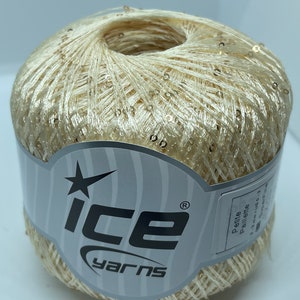 May include: A skein of ivory yarn with gold sequins. The yarn is wrapped around a cardboard tube with a label that says "Ice Yarns" and "Petite Pellette".