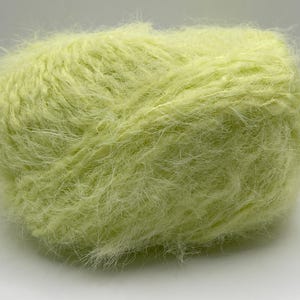 Könnte beinhalten: Ein Knäuel weiches, hellgrünes Garn mit einer flauschigen Textur. Das Garn scheint aus einem flauschigen Material zu bestehen, perfekt für Strick- oder Häkelprojekte. Die Farbe ist ein helles, frühlingshaftes Grün.