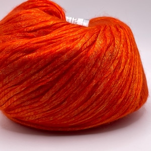 Puede incluir: Una madeja de hilo naranja vibrante, bien enrollada y texturizada. El hilo parece ser una fibra fina y suave, ideal para proyectos de tejido o ganchillo. El color brillante sugiere un producto final audaz y llamativo.