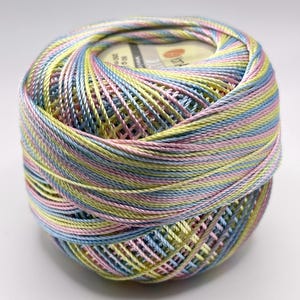 May include: A ball of colorful yarn in pastel shades of pink, blue, yellow, and green. The yarn is tightly wound, with visible layers and a textured surface. The label shows the weight of the yarn.