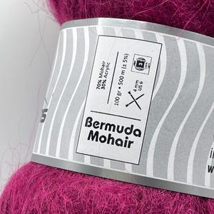 May include: A close-up of a vibrant magenta yarn ball labeled "Bermuda Mohair." The label indicates the yarn is 70% Mohair and 30% Acrylic, with a weight of 100 grams and a length of 500 meters. The recommended needle size is US 6, 4 mm.
