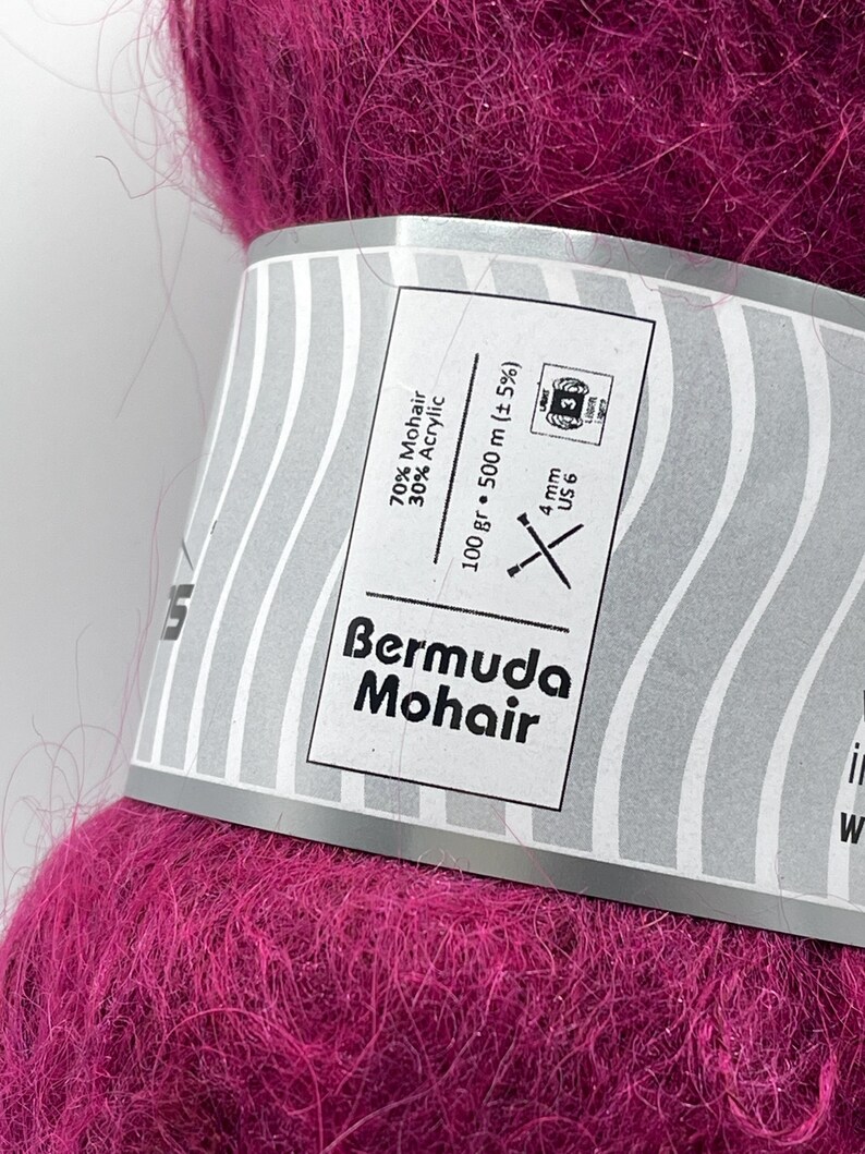 May include: A close-up of a vibrant magenta yarn ball labeled "Bermuda Mohair." The label indicates the yarn is 70% Mohair and 30% Acrylic, with a weight of 100 grams and a length of 500 meters. The recommended needle size is US 6, 4 mm.