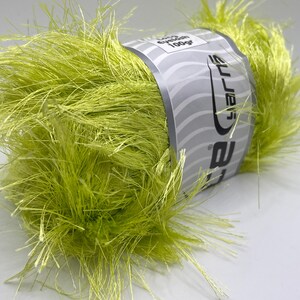 May include: A vibrant ball of lime green eyelash yarn. The yarn has a fluffy, textured appearance with long, wispy fibers extending outwards. A label wrapped around the center displays the brand name and weight, 100g. Ideal for knitting and crochet projects.