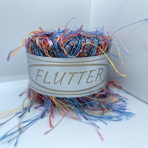 May include: A skein of multi-colored yarn with a label that reads "FLUTTER". The yarn is a mix of blue, red, yellow, and pink.
