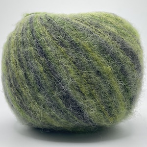 Puede incluir: Una madeja de hilo en tonos verdes, grises y negros. El hilo tiene una textura difusa y parece estar hecho de un material suave. La madeja es redonda y se asienta sobre un fondo blanco. Ideal para proyectos de tejido y ganchillo.