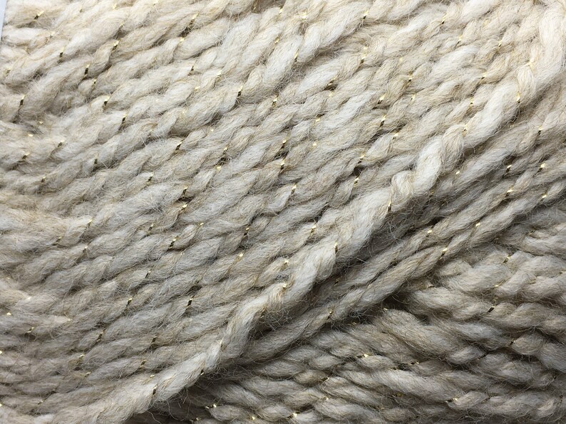 May include: Close-up of a beige yarn with gold metallic threads woven throughout.