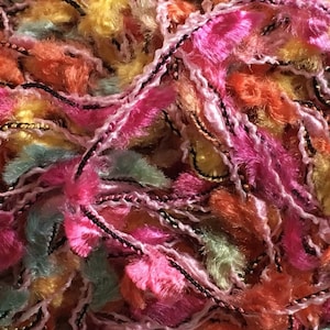 May include: A close-up of a multi-colored yarn with pink, orange, yellow, and green strands. The yarn has a fuzzy texture and is interwoven with a thin black thread and a gold thread.