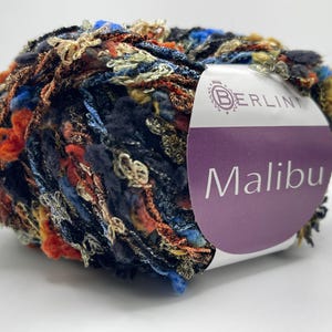 May include: A ball of colorful yarn with a mix of blue, orange, and gold threads. The yarn has a textured, fringed appearance. The label reads "Malibu" in white text on a purple background.