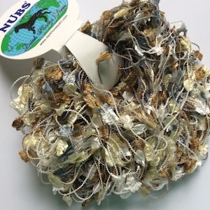May include: A skein of NUBS Daim Horse Yarn in a mix of gold, silver, and cream colors. The yarn is a chunky, fluffy texture with a metallic sheen.