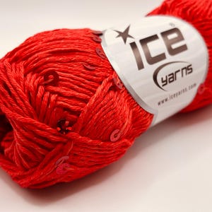 May include: A ball of bright red yarn with embedded sequins. The yarn is wrapped around a label that reads "ICE YARNS". The yarn is a solid colour, suitable for knitting or crochet projects. The label also includes the website address.