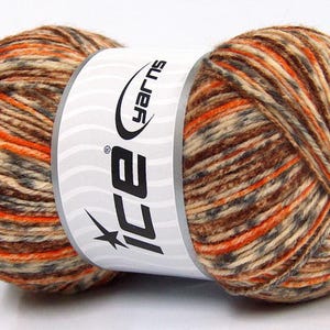 Op de afbeelding: Een bol veelkleurig garen in bruin, oranje, beige en grijstinten. Het garen is gewikkeld rond een wit etiket met de tekst "ice yarns" en een sterlogo. Geschikt voor brei- en haakprojecten.