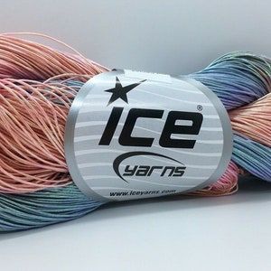 Pode incluir: Um novelo de fio iridescente em tons de rosa, azul e roxo. O fio está enrolado em torno de um rótulo que diz "ICE yarns" e "www.iceyarns.com".