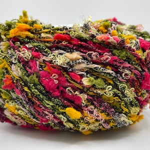 May include: A ball of multi-coloured yarn with a textured, looped design. The yarn features a mix of vibrant colours, including pink, green, yellow, and orange. Suitable for various crafting projects.