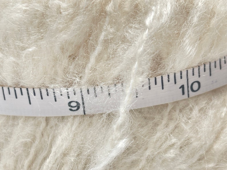 May include: A close-up of a white yarn skein with a measuring tape wrapped around it. The tape reads "9" and "10".