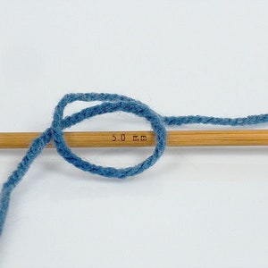 May include: A close-up of blue yarn wrapped around a wooden knitting needle with the text "5.0 mm" printed on the needle.