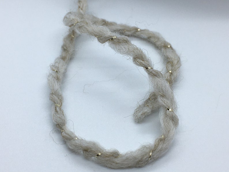 May include: A close-up of a beige yarn with gold glitter thread woven throughout. The yarn is twisted into a loop.