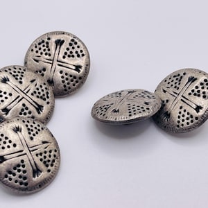 Puede incluir: Colección de botones antiguos de color plateado. Cada botón es redondo con un diseño de cruz y pequeños detalles de puntos. Los botones están dispersos sobre una superficie blanca, mostrando sus intrincados patrones y apariencia envejecida.