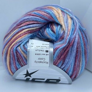 May include: A ball of variegated yarn featuring a blend of blue, pink, and peach tones. A white paper label is wrapped around the center, displaying the text Rockabilly Color, 4-6 mm / US 6-8, Medium, and 50g 125m 67% Tencel 33% Polyamide.