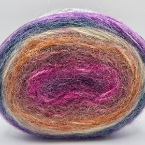 Può includere: Un gomitolo di lana colorato con una sfumatura di colori, tra cui viola, arancione, blu e crema. Il filato appare morbido e soffice, ideale per progetti di maglia o uncinetto. Il gomitolo misura circa 10 cm di diametro.