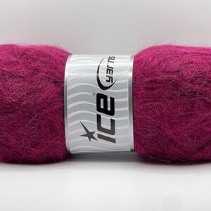 May include: A vibrant magenta yarn ball with a silver and white label. The label features the brand name "ICE" and a starburst design. The yarn appears soft and fluffy, ideal for knitting or crocheting projects.
