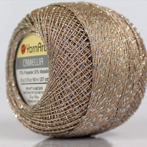 May include: A skein of beige yarn with silver metallic thread. The label reads "YarnArt" and "Camellia" with the yarn composition: 70% Polyester 30% Metallic. 35g (1.2 oz) 190 m (207 yds).