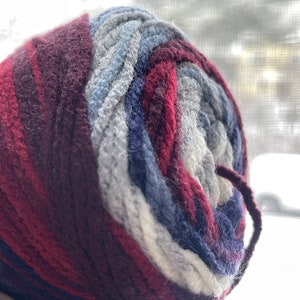 May include: A ball of yarn with a multi-colored pattern of burgundy, gray, blue, and white.