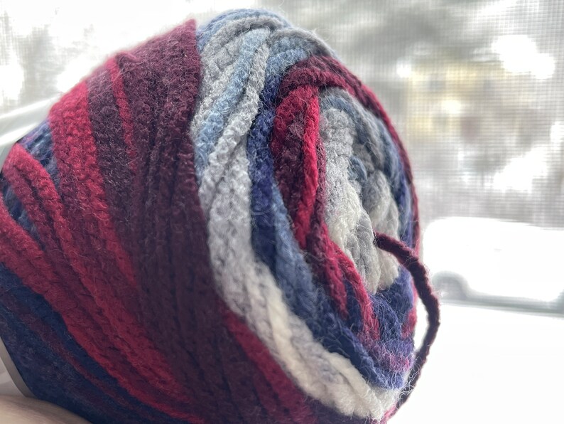 May include: A ball of yarn with a multi-colored pattern of burgundy, gray, blue, and white.