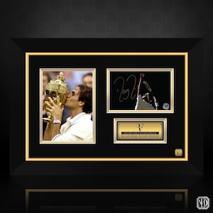 Puede incluir: Exhibición enmarcada con imágenes de Roger Federer. Incluye una foto de Federer besando un trofeo, una imagen firmada y una placa con su nombre y títulos. El marco es negro con detalles dorados.