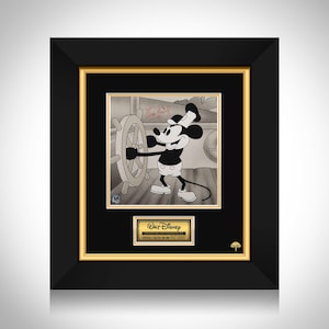 Op de afbeelding: Ingelijste zwart-wit kunstwerk met Mickey Mouse aan het roer van een schip. Het kunstwerk zit in een zwarte lijst met een gouden binnenrand. Een gouden plaatje onderaan luidt "Walt Disney" en "Producer & Creator, His Own Walt Disney".