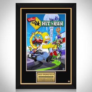 Może przedstawiać: Oprawiona grafika przedstawiająca Homera Simpsona z Simpsonów biegnącego w scenie z gry wideo "Hit & Run". Grafika zawiera tytuł gry, podpisy postaci i tabliczkę "Save Springfield!". Rama jest czarna ze złotą wewnętrzną obwódką.