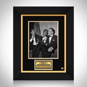 Peut inclure: Photographie encadrée en noir et blanc de Dean Martin, Sammy Davis Jr. et Frank Sinatra, tous en smoking, riant. La photo est dans un cadre noir avec un bord intérieur doré. Une plaque dorée en dessous indique "Ratpack".
