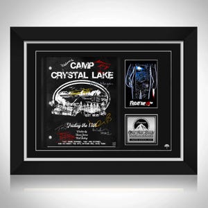 May include: Framed artwork with a black frame, featuring a Camp Crystal Lake design and the text "Friday the 13th." Includes a smaller image and a Paramount Pictures logo. The frame is black.