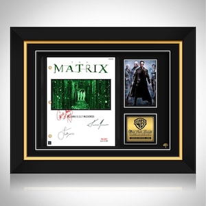 May include: Framed The Matrix movie memorabilia. The frame is black with a gold inner border. The display includes a script page, a movie still, and a Warner Bros. seal. The script page has the movie title and signatures.