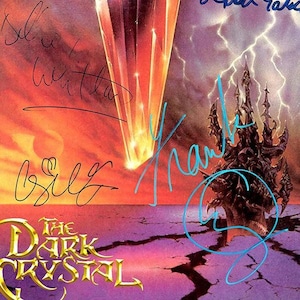 Puede incluir: Ilustraci&oacute;n de "Cristal Oscuro" que representa una escena fant&aacute;stica con un castillo, rel&aacute;mpagos y un haz de luz. La obra de arte tiene un tema de fantas&iacute;a con una paleta de colores naranja, morado y dorado. Varias firmas son visibles.