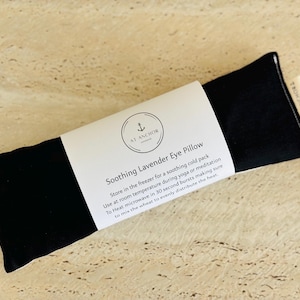 May include: A rectangular black eye pillow wrapped in a white paper band labelled At Anchor Soothing Lavender Eye Pillow. The text provides instructions for cold storage, room temperature use, and microwave heating in 30-second bursts.