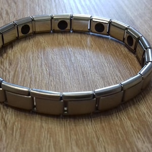 Peut inclure: Un bracelet magnétique en argent avec plusieurs maillons. Le bracelet a des inserts magnétiques noirs.