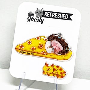 Peut inclure: Une carte blanche avec une illustration d'une fille endormie et d'un chat. La fille est dans une couverture jaune avec des fleurs rouges. Le chat est jaune avec des taches marron. Le texte sur la carte indique "Our Girl Ghosty REFRESHED" et "©1983 OAA INC."