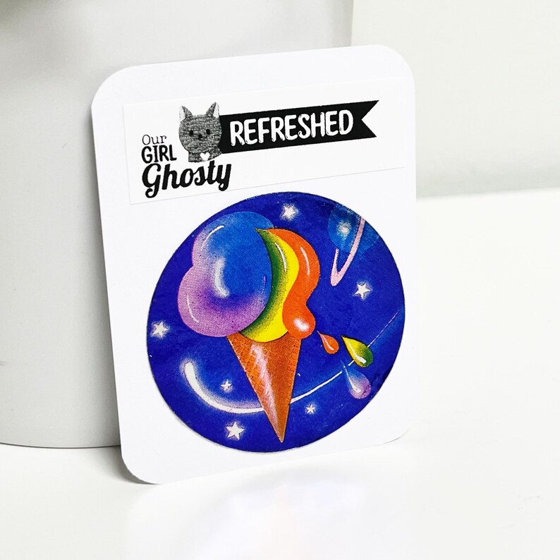 May include: A white sticker featuring a vibrant ice cream cone illustration. The ice cream is depicted in rainbow hues, set against a blue backdrop with stars. The sticker also includes the text "Our Girl Ghosty" and "Refreshed".
