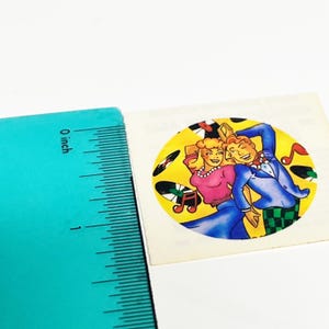 May include: A vintage-style sticker featuring a couple dancing in a retro style. The sticker is round with a yellow background and includes musical notes and vinyl records. The couple is dressed in pink, blue, and white attire.