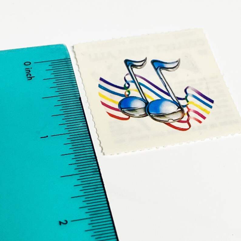 May include: A postage stamp featuring two blue musical notes with rainbow-colored ribbons. The stamp is approximately 1 inch in height. The background is white, and the stamp has a perforated edge.