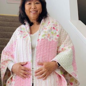 May include: A quilted jacket in shades of pink, white, and green. The jacket features a patchwork design with floral and geometric patterns. The sleeves are wide and the jacket is open in the front.