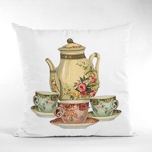 Puede incluir: Una almohada blanca con una ilustraci&oacute;n vintage de una tetera y tres tazas de t&eacute;. La tetera y las tazas est&aacute;n decoradas con motivos florales en tonos rosa, verde y amarillo.