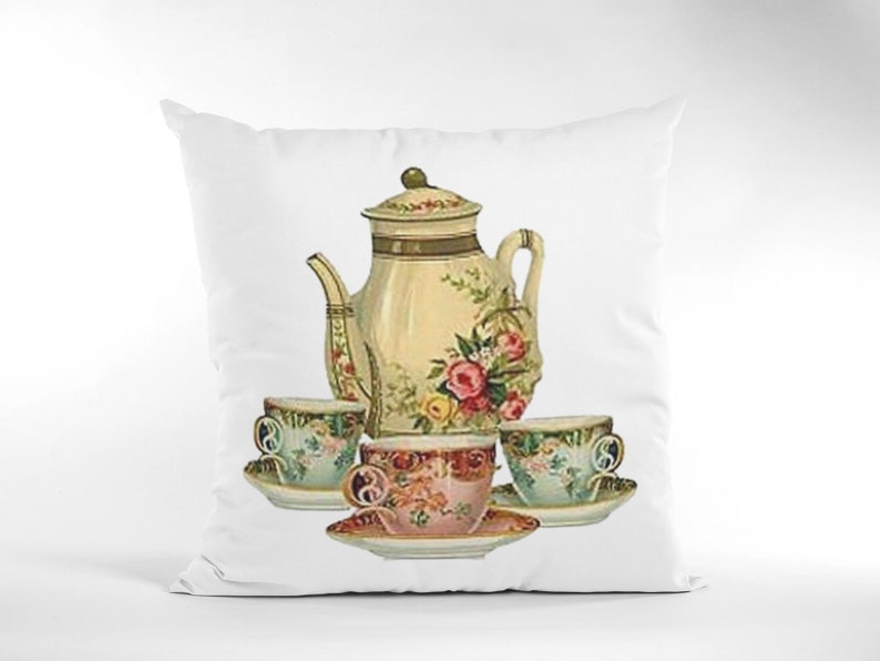 Puede incluir: Una almohada blanca con una ilustraci&oacute;n vintage de una tetera y tres tazas de t&eacute;. La tetera y las tazas est&aacute;n decoradas con motivos florales en tonos rosa, verde y amarillo.