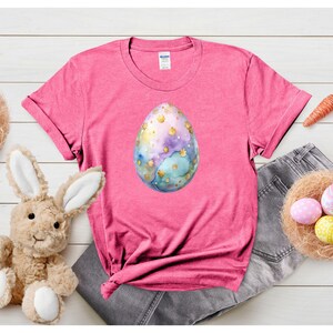 May include: Pink t-shirt with a watercolor Easter egg design. The egg is blue, green, and gold with white speckles.