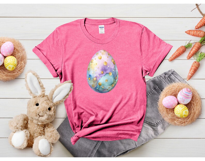 May include: Pink t-shirt with a watercolor Easter egg design. The egg is blue, green, and gold with white speckles.