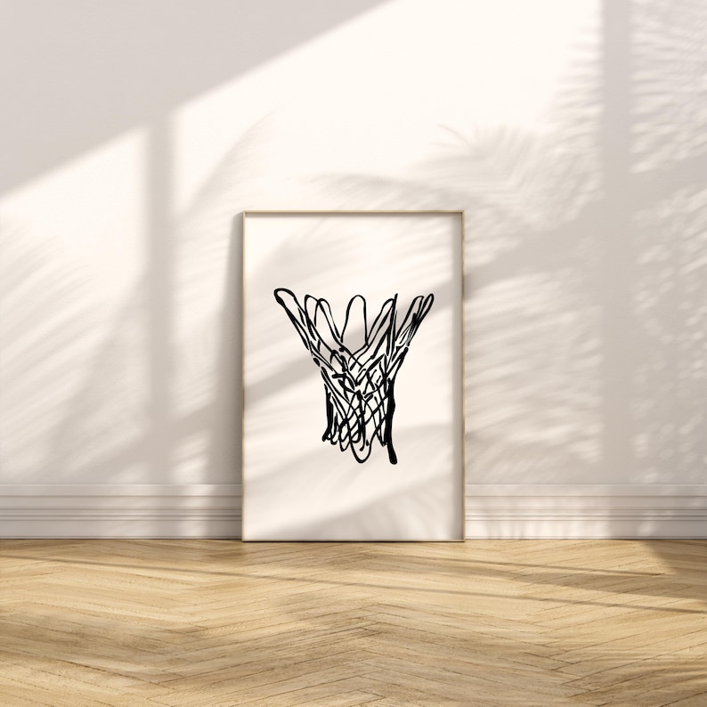 May include: A framed print featuring a black line drawing of a basketball net. The artwork is displayed against a white wall with shadows and a wooden floor. The minimalist design adds a modern touch to the space.