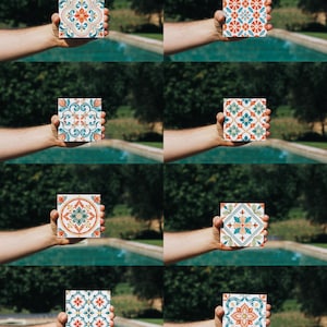 Op de afbeelding: Een verzameling van acht vierkante keramische tegels, elk met een eigen decoratief patroon in tinten oranje, blauwgroen en wit. De ontwerpen bevatten ingewikkelde bloemmotieven, geometrische vormen en symmetrische krulwerkarrangementen.