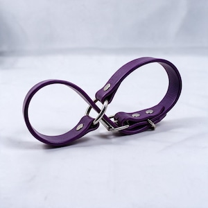 A purple leather strap with metal buckles and clips is shown against a white background.
