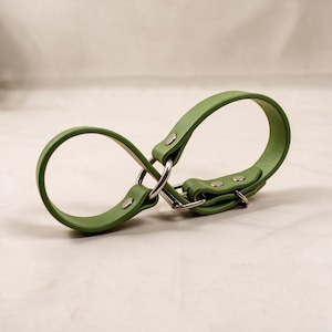 A green leather strap with metal buckles and clips is shown against a light background.